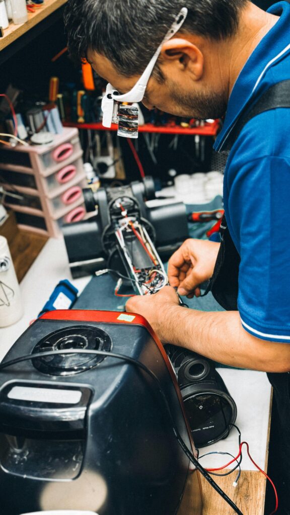 pexels-photo-31869841-31869841 A technician carefully repairs a vacuum cleaner in a cluttered workshop, showcasing skilled craftsmanship.
